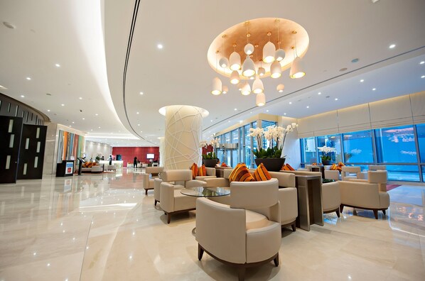 A modern hotel lobby with a curved ceiling, a reception desk, and seating areas with round tables.