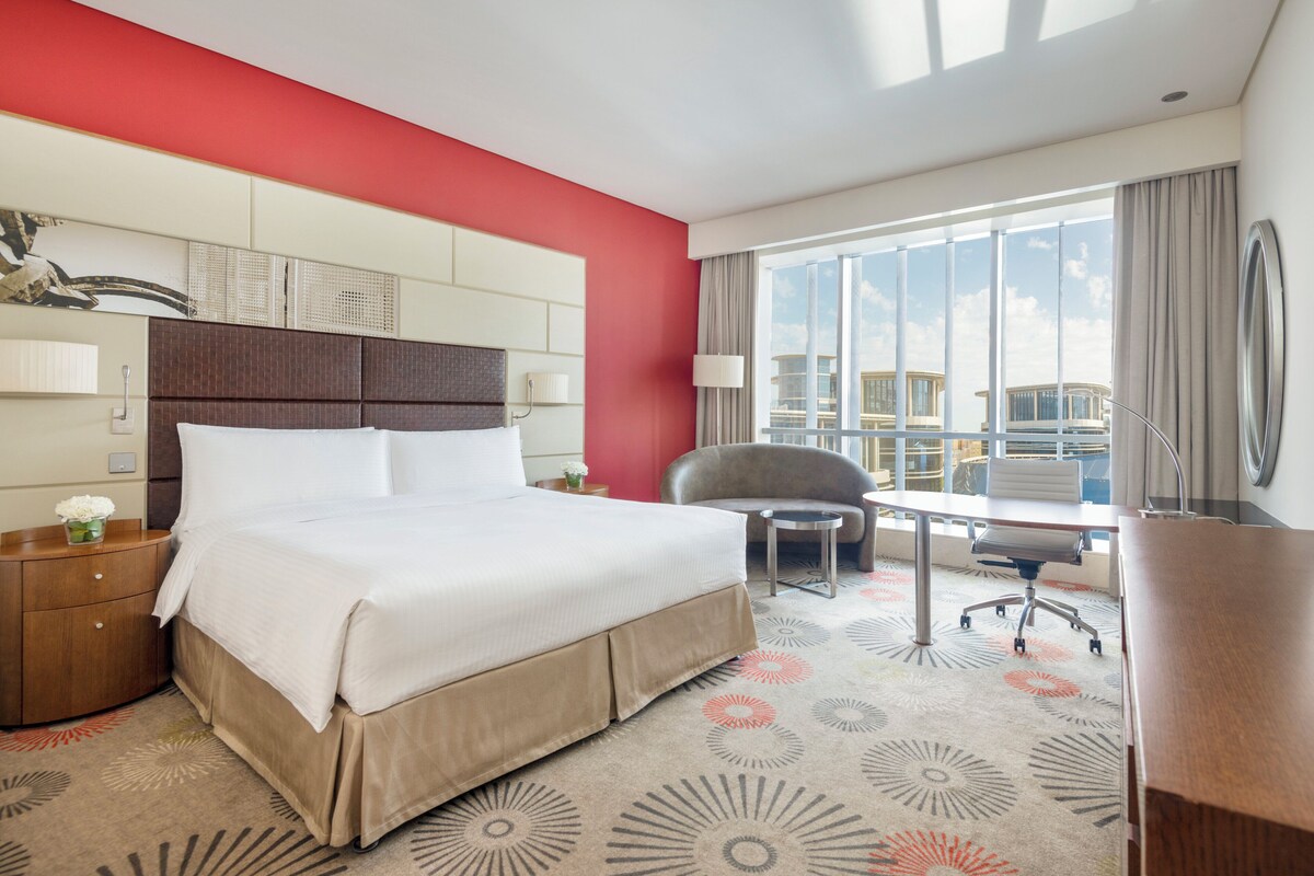 A hotel room with a large bed, a desk, a chair, and a view of the city.