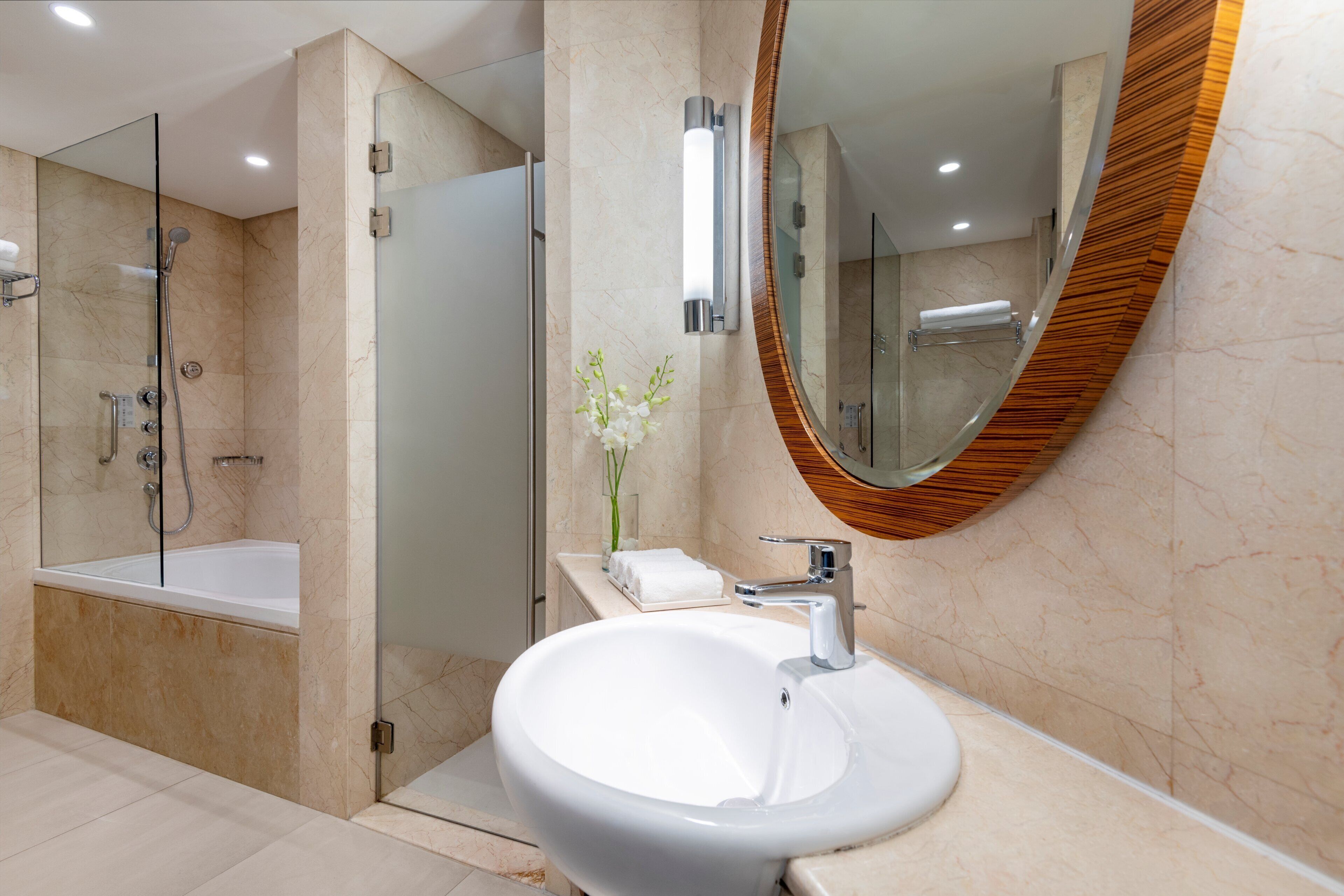 Un baño moderno con un lavabo grande, cabina de ducha con paredes de vidrio y espejo con marco de madera.