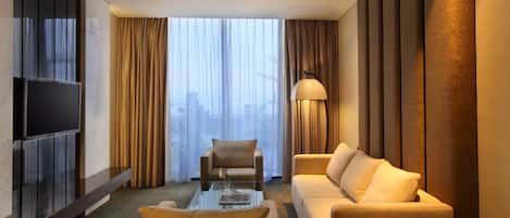 A modern hotel room with a large window, a flat-screen TV, a sofa, a coffee table, and a lamp.