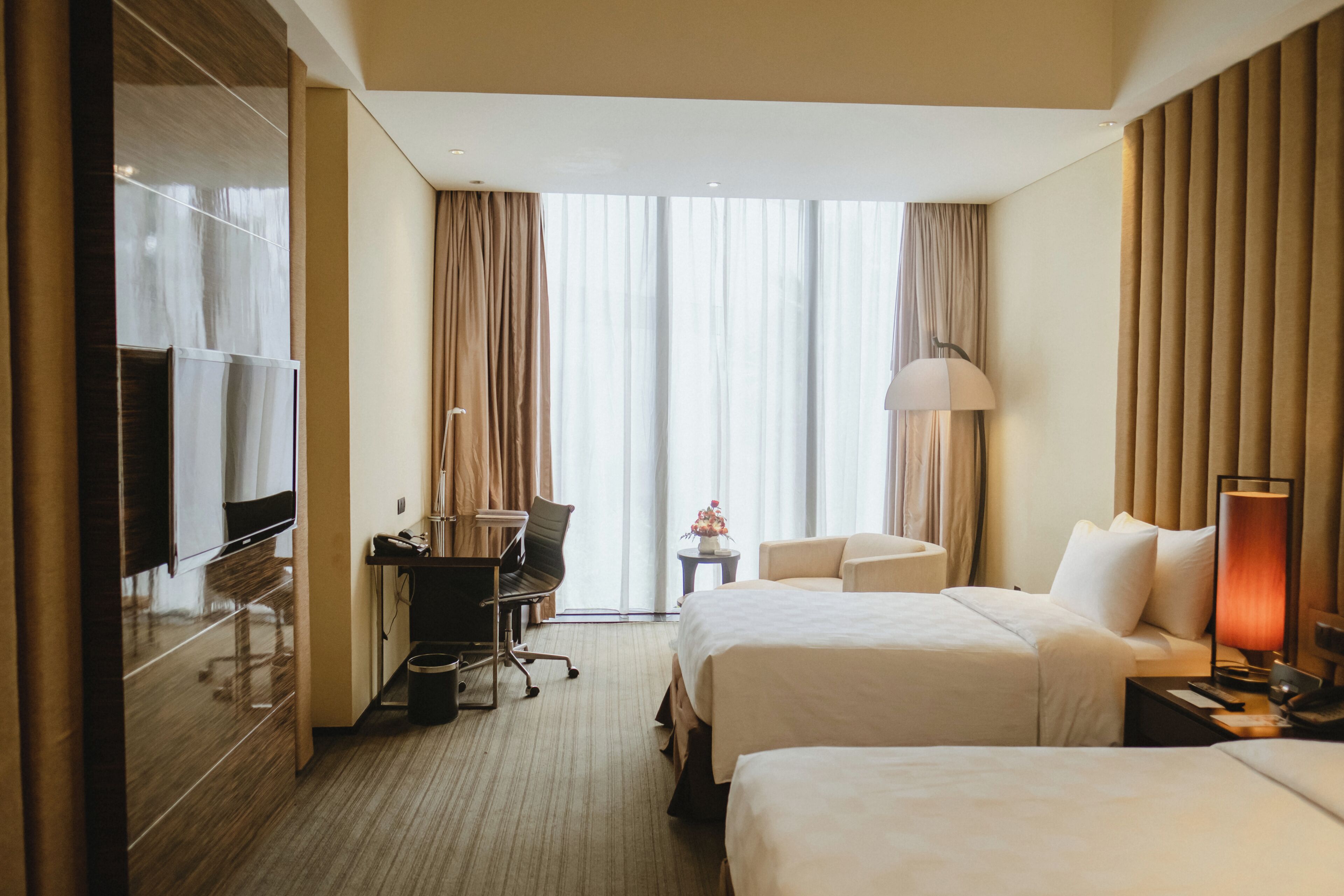 A hotel room with two beds, a desk with a chair, a television, and a lamp.