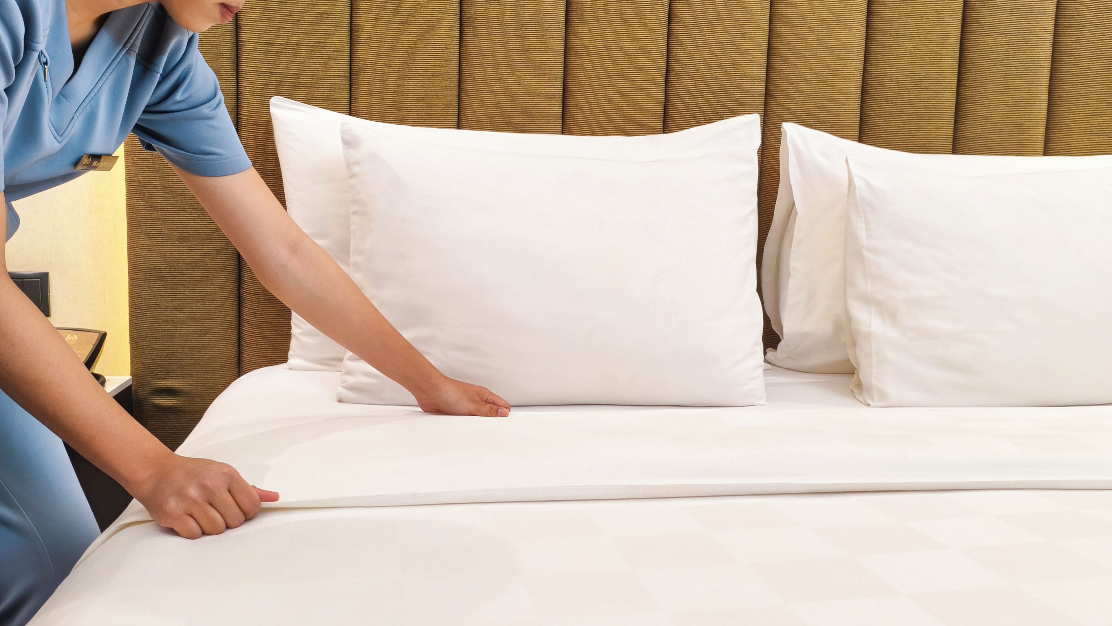 A person adjusting a white pillow on a bed with a headboard.