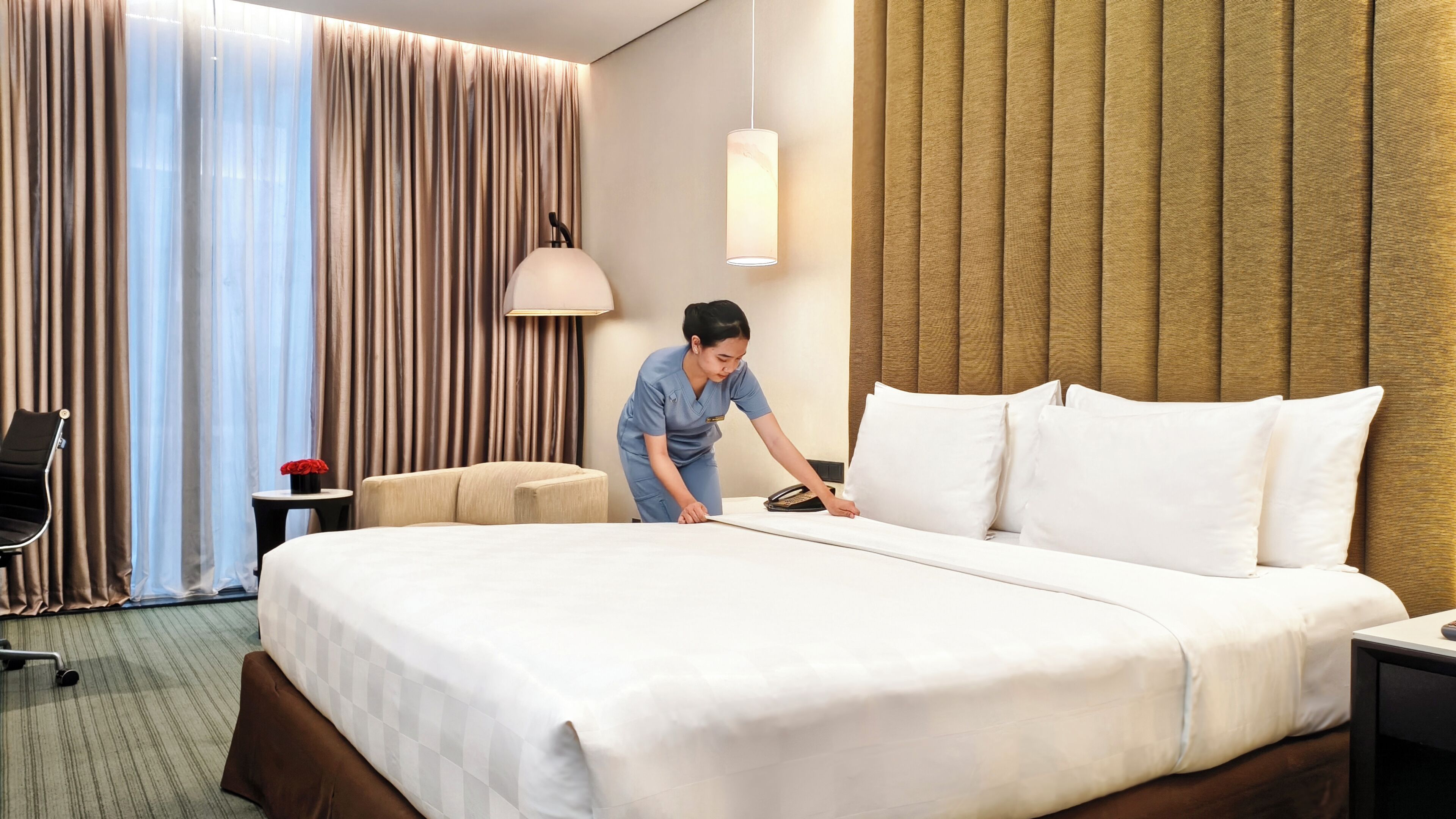 A hotel room with a bed, a desk, a chair, a lamp, and a curtain.