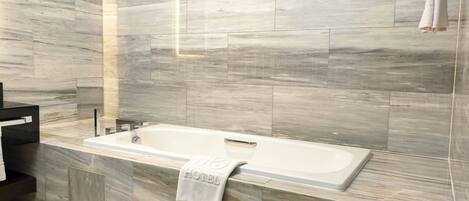 A modern bathroom with a marble wall, a bathtub, and a towel rack.