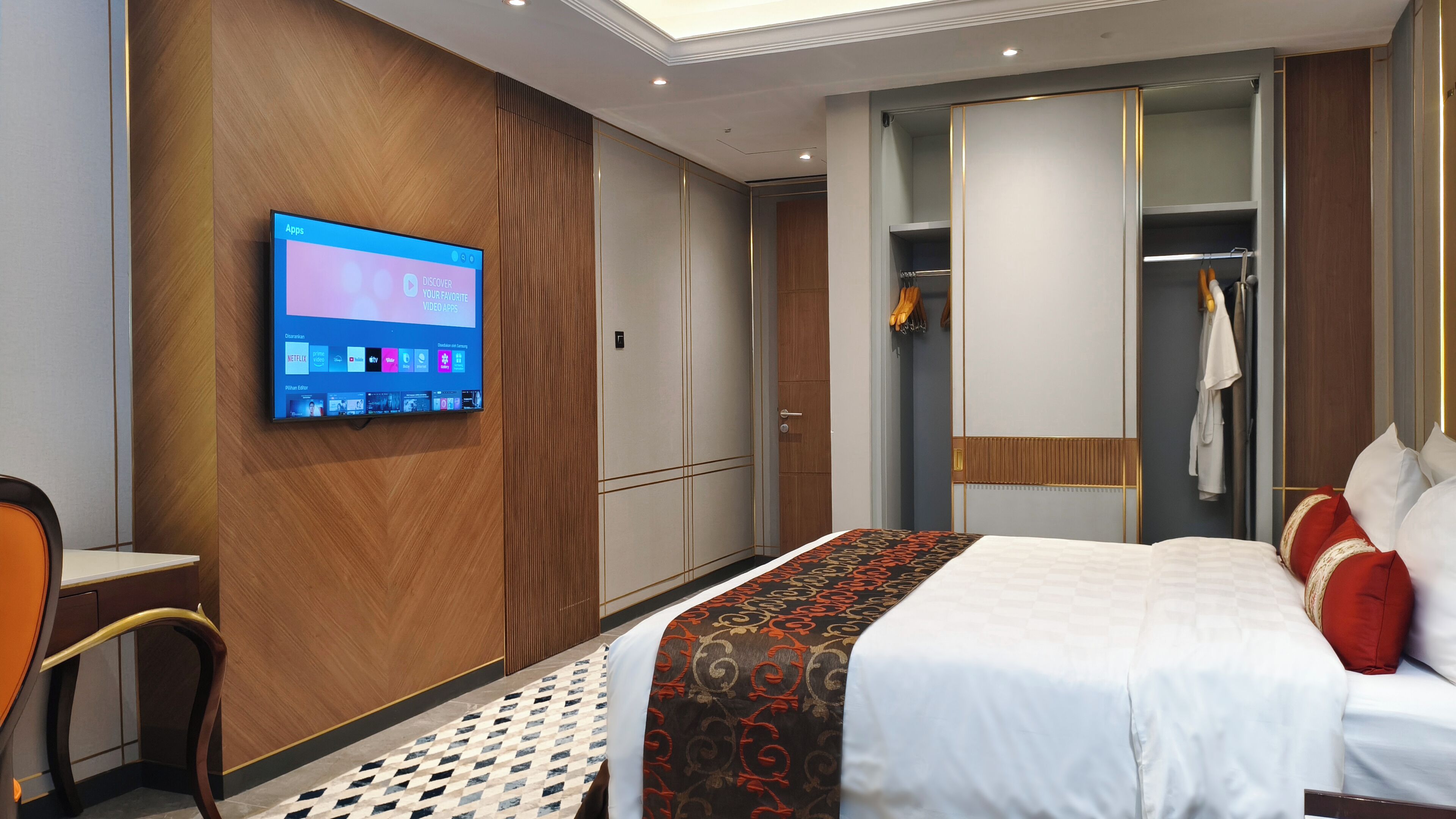 A hotel room with a bed, a TV mounted on the wall, a wardrobe, and a seating area.