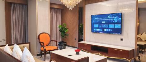 Una habitación de hotel moderna con un televisor de pantalla plana grande, asientos cómodos, una araña y una planta en maceta.