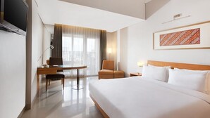 Una habitación de hotel con cama, escritorio, silla, televisión y ventana con cortinas.