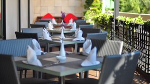 An outdoor dining area with tables set for two, featuring wicker chairs and a tiled wall in the background. - Hotel Santika Jemursari Surabaya (Surabaya)