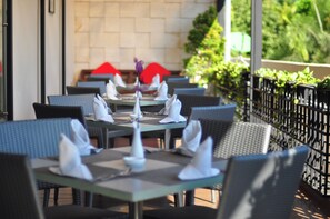 An outdoor dining area with tables set for two, featuring wicker chairs and neatly folded white napkins. - Hotel Santika Jemursari Surabaya (Surabaya)