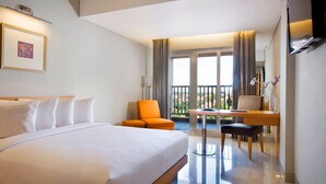 Habitación de hotel con una cama grande, un escritorio con silla, televisión y balcón con cortinas.