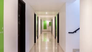 Un pasillo moderno de hotel con suelo brillante, paredes de acento verde y puertas de marco negro.