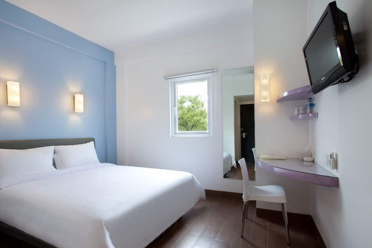Habitación de hotel con cama, escritorio, silla, televisión y ventana.