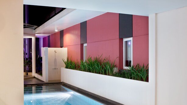 Un área de piscina interior moderna con pared de vidrio, ducha y pared vegetal.