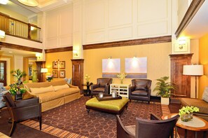 A spacious lobby with a high ceiling, a central seating area with a sofa and chairs, a coffee table, and a decorative vase with flowers. - Holiday Inn Express and Suites Williston by IHG (Williston)