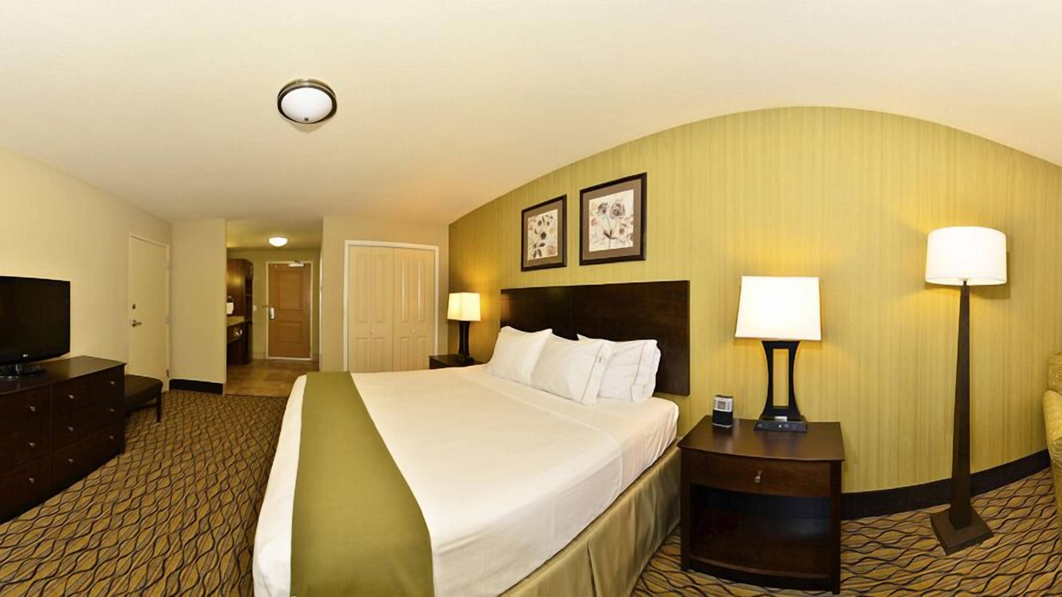 A hotel room with a large bed, two bedside lamps, a flat-screen TV, and a small table.