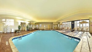 A large indoor swimming pool with lounge chairs and sunbeds around the perimeter, a reception area with a counter and chairs, and large windows providing natural light. - Holiday Inn Express and Suites Williston by IHG (Williston)