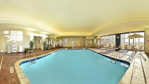 A large indoor swimming pool with lounge chairs and sunbeds around the perimeter, a reception area with a counter and chairs, and large windows providing natural light. - Holiday Inn Express and Suites Williston by IHG (Williston)