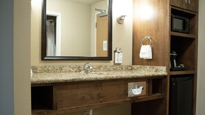 A bathroom with a granite countertop, a sink, a mirror, a towel rack, a microwave, and a cabinet. - Holiday Inn Express and Suites Williston by IHG (Williston)