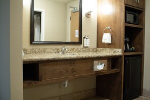 A bathroom with a granite countertop, a sink, a mirror, a towel rack, a microwave, and a cabinet. - Holiday Inn Express and Suites Williston by IHG (Williston)