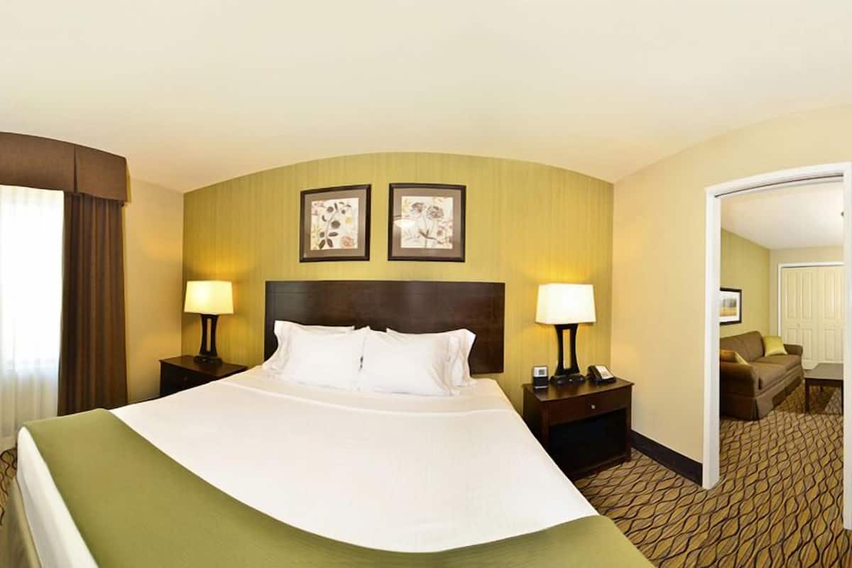 A hotel room with a large bed, two bedside tables with lamps, a headboard, and two framed pictures on the wall.