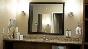A bathroom with a granite countertop, a sink, a mirror, a hairdryer, and toiletries. - Holiday Inn Express and Suites Williston by IHG (Williston)