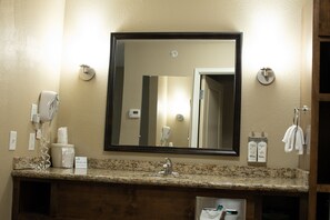 A bathroom with a granite countertop, a sink, a mirror, a hairdryer, and toiletries. - Holiday Inn Express and Suites Williston by IHG (Williston)