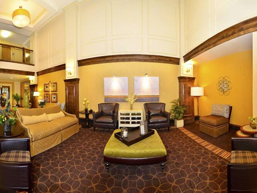 A spacious lobby with a high ceiling, a central seating area with a sofa and chairs, and a patterned carpet.