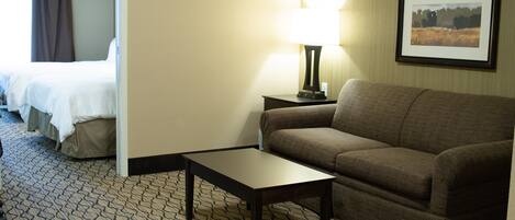 A hotel room with a bed, a sofa, a small table, a lamp, and a framed picture on the wall.