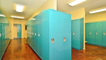 A hallway with rows of teal lockers, wooden flooring, and fluorescent ceiling lights.
