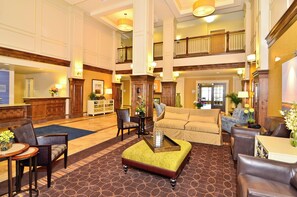 A spacious lobby with a high ceiling, a central seating area with a yellow ottoman, and a reception desk. - Holiday Inn Express and Suites Williston by IHG (Williston)