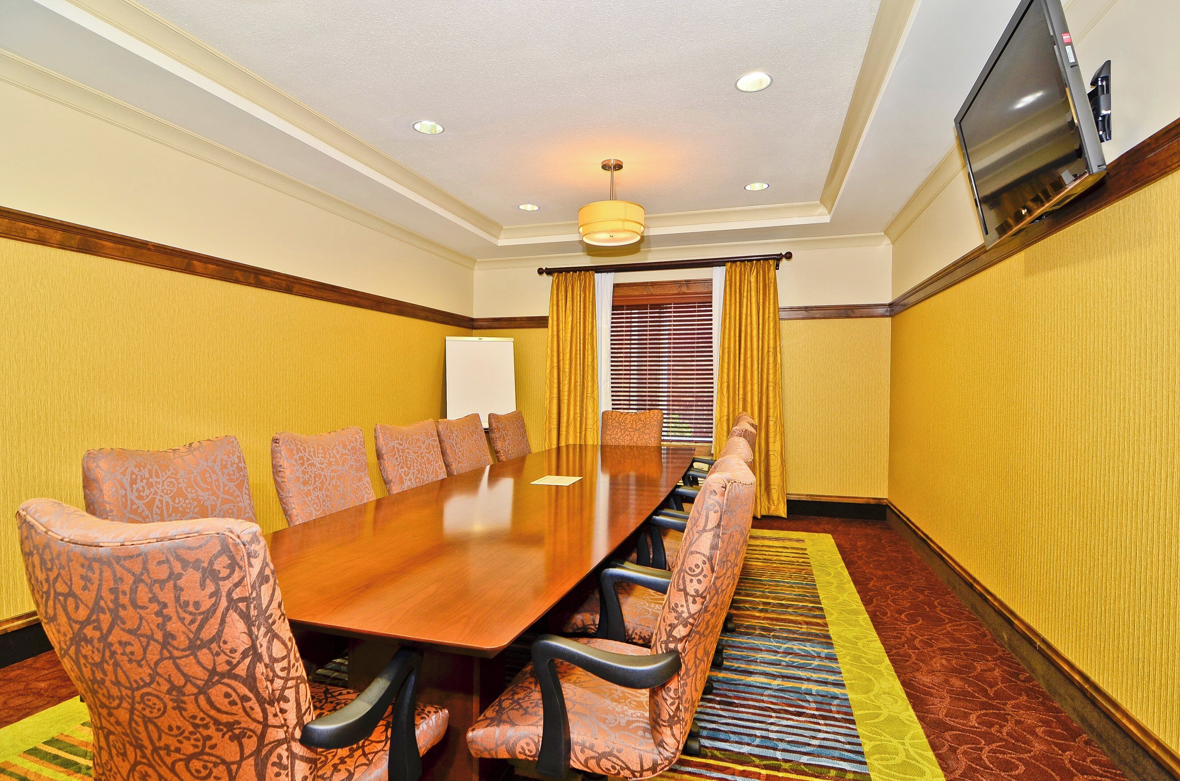 Un salón de conferencias con una larga mesa, sillas estampadas, una pizarra y un televisor.