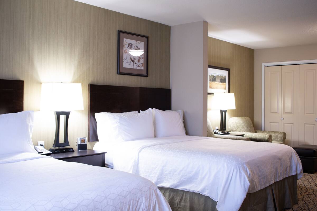 A hotel room with two beds, bedside tables with lamps, a chair, and a wardrobe.
