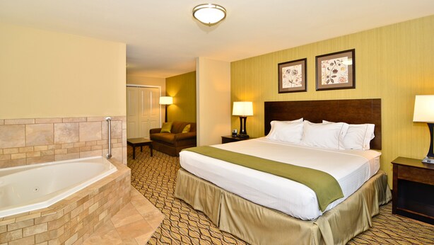 A hotel room with a large bed, a separate bathroom with a bathtub, a chair, two bedside lamps, and framed artwork on the wall. - Holiday Inn Express and Suites Williston by IHG (Williston)