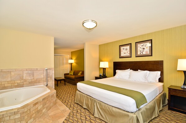 A hotel room with a large bed, a separate bathroom with a bathtub, a chair, two bedside lamps, and framed artwork on the wall. - Holiday Inn Express and Suites Williston by IHG (Williston)