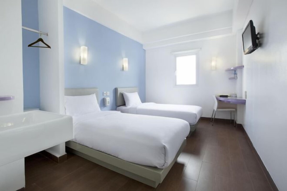 Habitación de hotel con dos camas, un escritorio, una silla, un televisor montado en la pared y una ventana.
