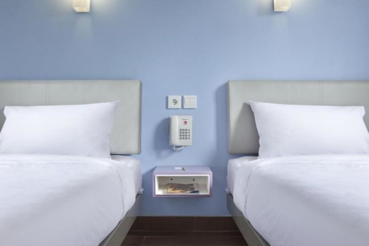 A hotel room with two beds, a wall-mounted phone, and a small storage box.