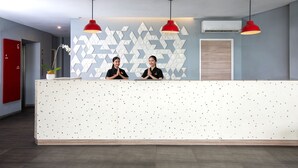 A reception desk with two staff members, a geometric patterned wall, and red pendant lighting. - Amaris Hotel - Bandara Soekarno Hatta (Tangerang)