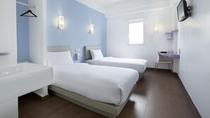 A hotel room with two beds, a desk, a chair, a sink, and a TV mounted on the wall. - Amaris Hotel - Bandara Soekarno Hatta (Tangerang)