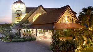 Un hotel con una torre destacada, un acceso cubierto y abundante vegetación.