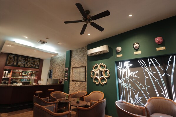 Un restaurant doté d’un bar, de chaises en bois, d’un ventilateur de plafond, d’œuvres d’art décoratives sur les murs et d’un appareil de climatisation.