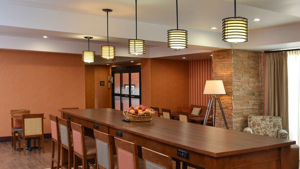 A hotel dining area with a long wooden bar, bar stools, and hanging pendant lights. - Hampton Inn Ottumwa (Ottumwa)