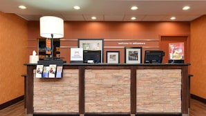 A reception desk with a stone facade, a welcome sign, framed pictures, a counter with brochures, and a lamp. - Hampton Inn Ottumwa (Ottumwa)