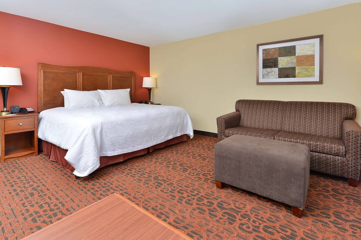A hotel room with a bed, a sofa, a small table, and a nightstand.