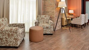 A hotel room with a sofa, armchair, ottoman, and a desk with a lamp. - Hampton Inn Ottumwa (Ottumwa)