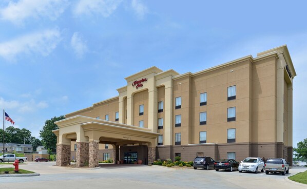 Un hotel Hampton Inn con fachada color beige, múltiples ventanas y entrada cubierta.