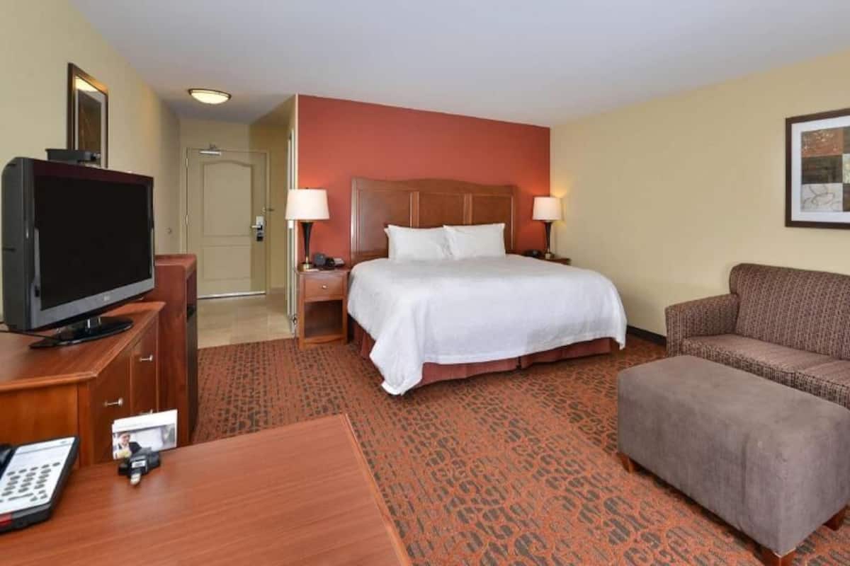 A hotel room with a bed, a television, a desk, a sofa, and a painting on the wall.