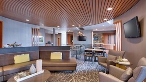 Een moderne hotel lobby met een zithoek, een eetruimte en een aan de muur bevestigde flatscreen televisie.