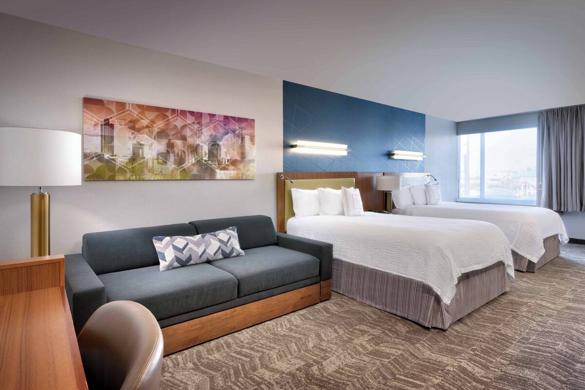 Ein Hotelzimmer mit einer Couch, einem Bett, einem Schreibtisch und einem Stadtbild.
