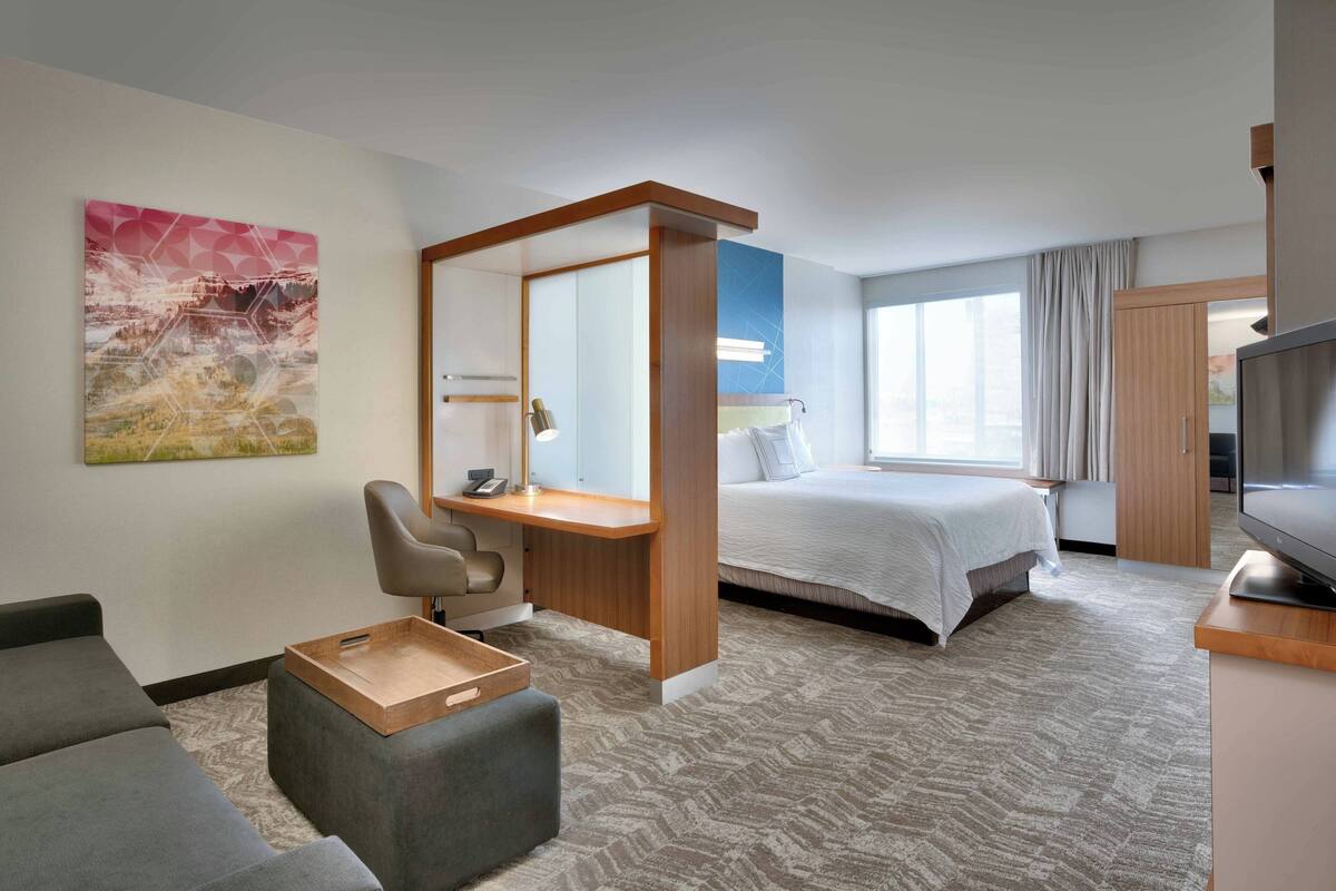 Ein modernes Hotelzimmer mit Bett, Schreibtisch mit Stuhl, Fernseher und großem Fenster.