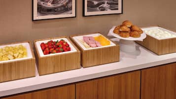 Un bufé con diversos alimentos, incluyendo frutas, fresas, jamón, queso y pasteles.